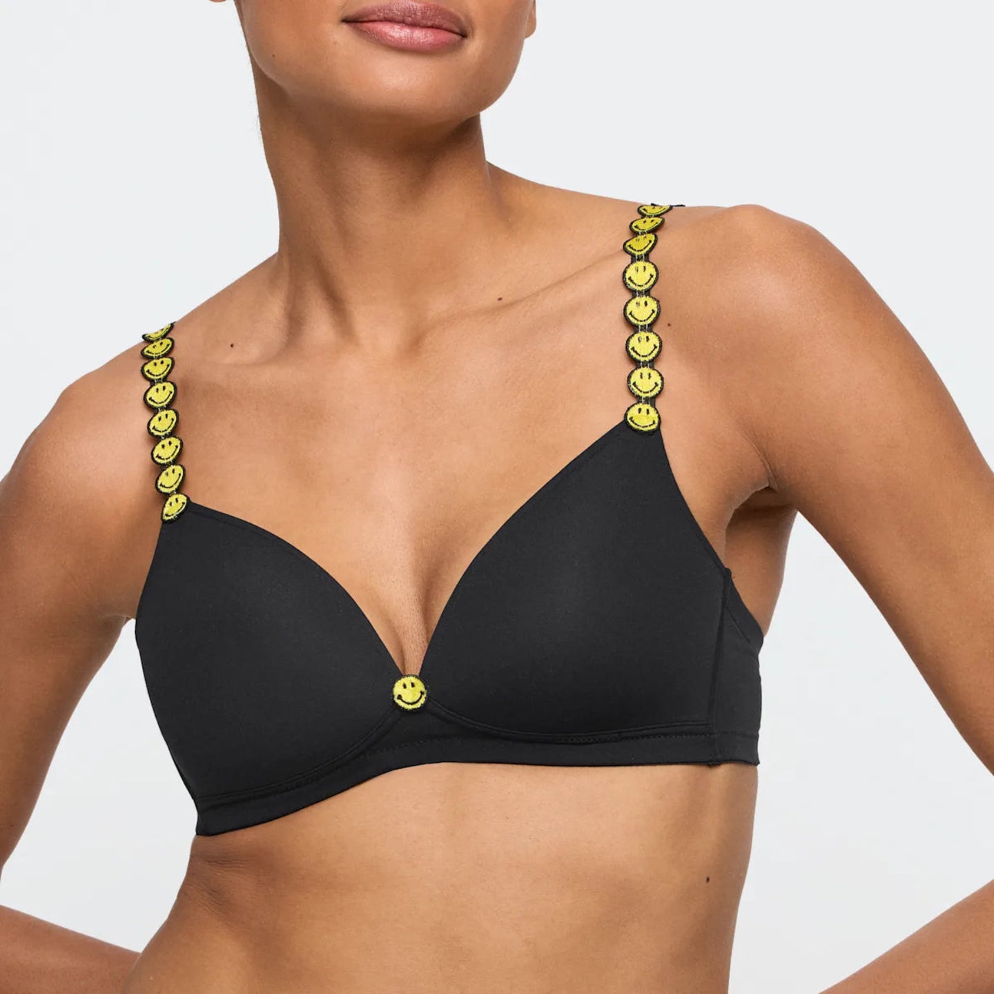 Black bikini top with smiley face straps on a plain background