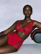 Load image into Gallery viewer, A model wearing a red lace and mesh lingerie set with matching brown gloves, posed against a light gray studio background.
