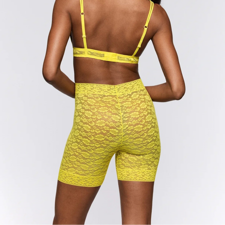 Woman wearing a yellow sports bra and shorts set on a plain background