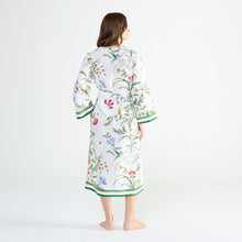 Load image into Gallery viewer, A woman viewed from the back wearing a white kimono-style robe with a colorful floral and bird print and green trim, standing barefoot against a plain white studio background.
