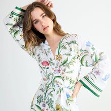 Load image into Gallery viewer, A woman modeling a white long-sleeve button-front shirt dress with a colorful botanical print and striped cuffs, posed against a light gray studio background.
