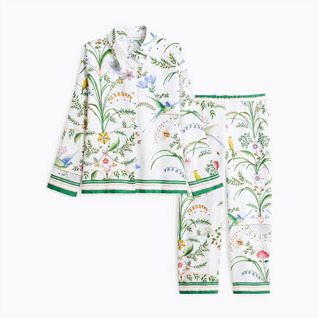 A two-piece pajama set featuring a long-sleeve button-up shirt and matching pants, both printed with a colorful botanical and bird pattern on a white background, finished with green striped trim.