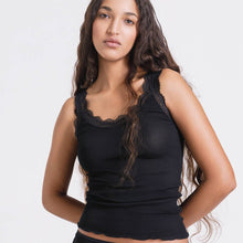 Load image into Gallery viewer, A woman modeling a black ribbed silk tank top with black calais lace trim along the scoop neckline and shoulder straps, set against a plain white studio background.
